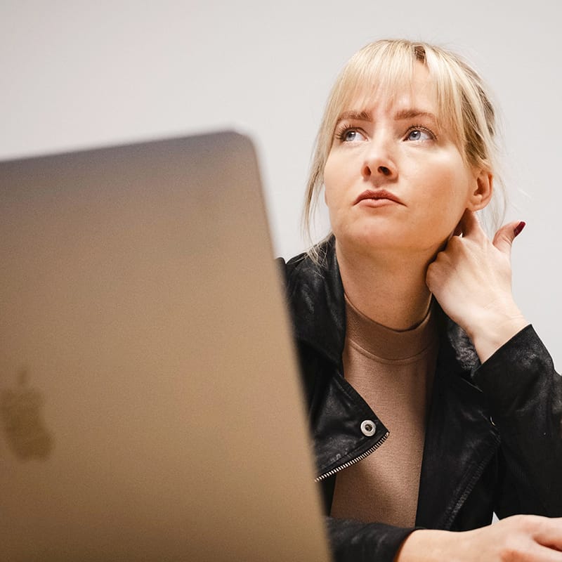 Thoughtful blonde woman looking up behind a MacBook laptop