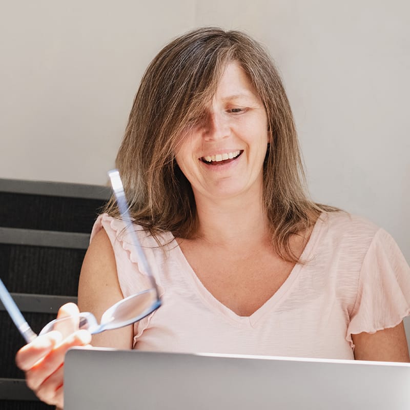 Smiling woman holding glasses while working on laptop