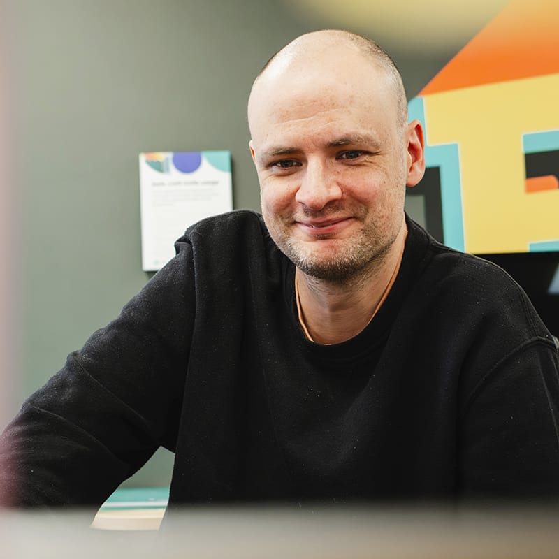 Smiling bald man in black jumper at office desk
