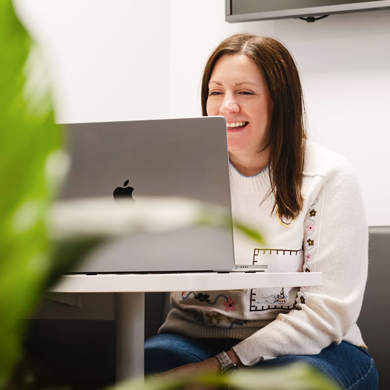 Woman smiling and working on Apple MacBook laptop in office