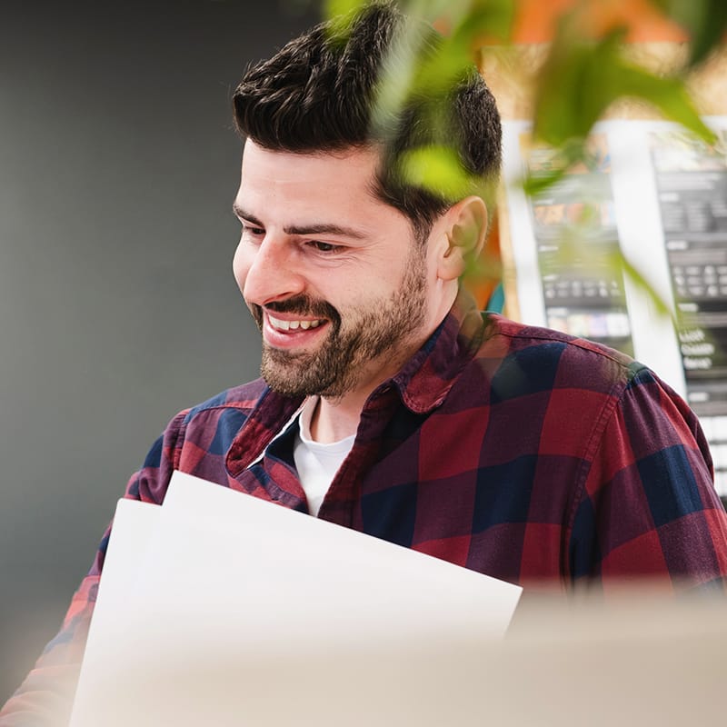 Smiling man in plaid shirt reviewing documents at office desk