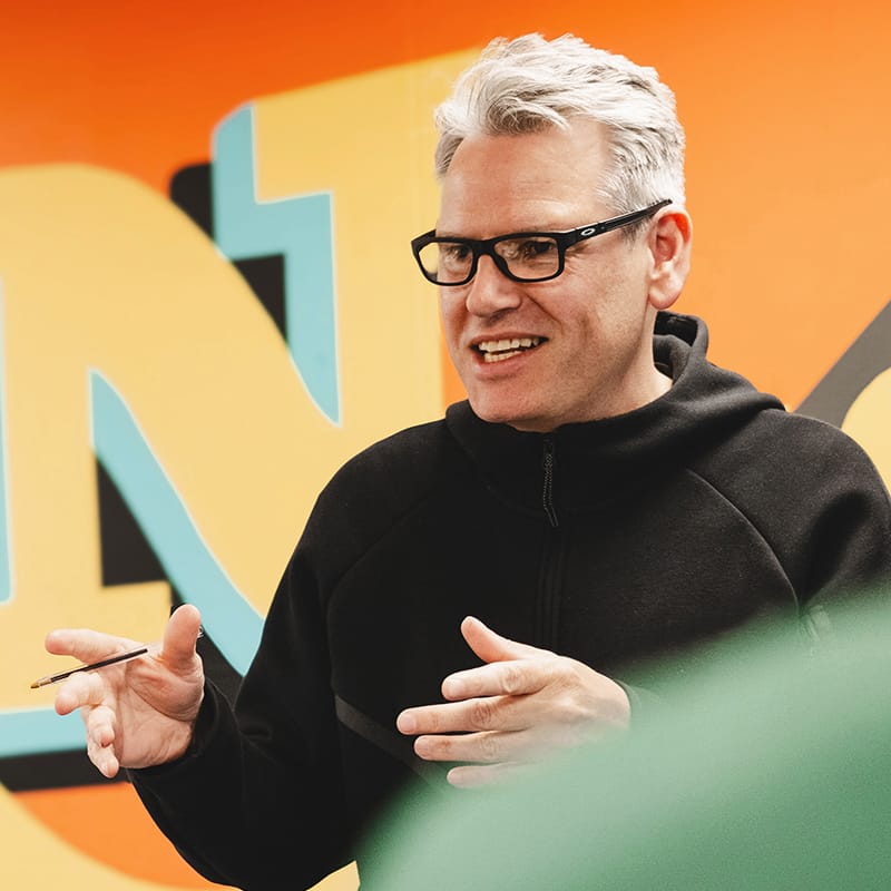 Man with glasses speaking animatedly holding a pencil