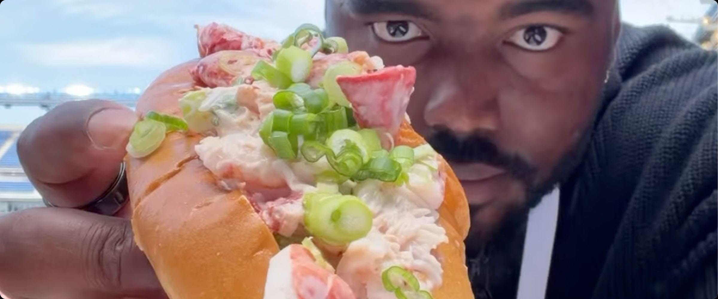 Man holding a lobster roll topped with spring onions