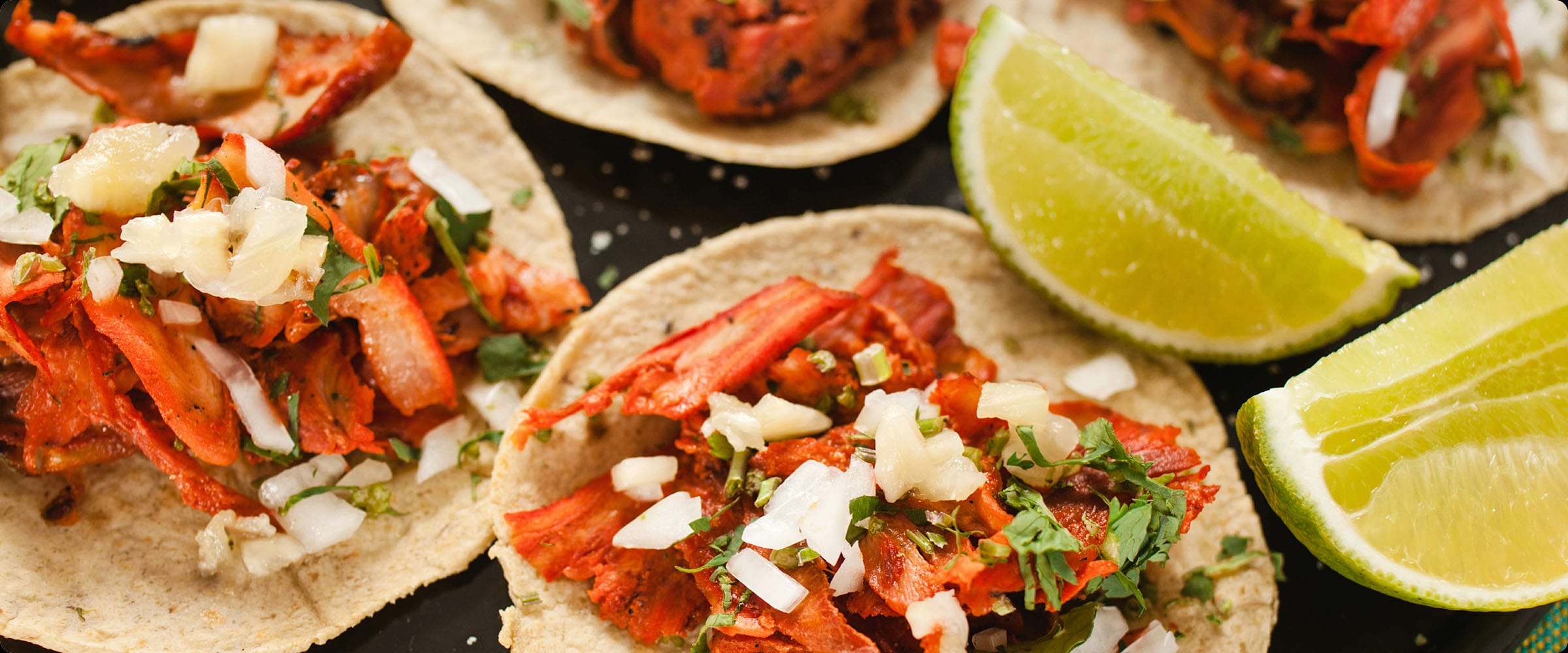 Mexican tacos al pastor with onion, coriander, and lime wedges
